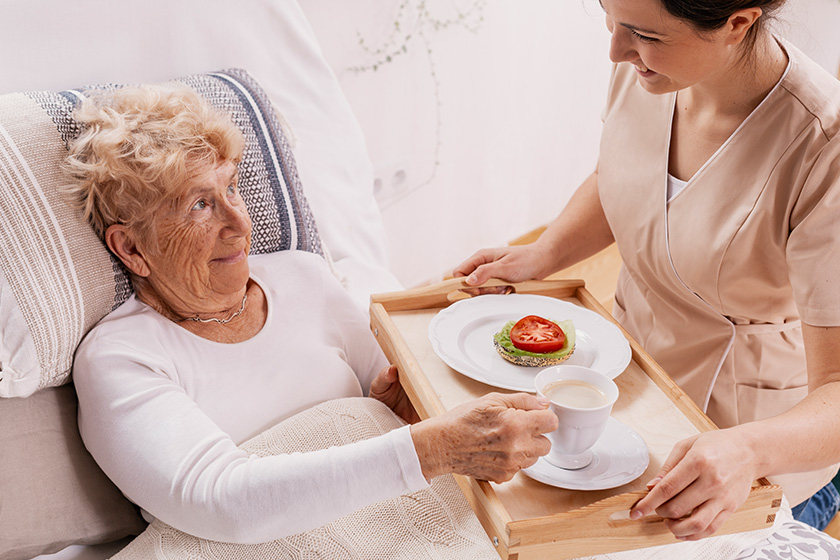 helpful volunteer in beige uniform serving coffee to senior female patient