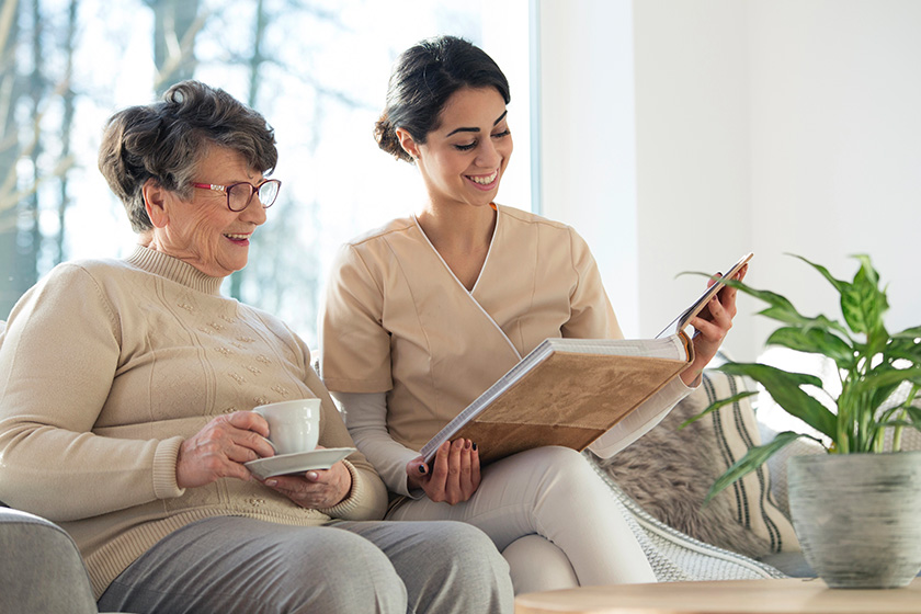 smiling professional caretaker showing family album elder woman living room