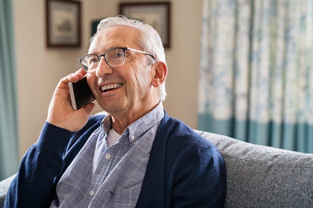 Smiling,Old,Man,Talking,Over,Smartphone,While,Relaxing,At,Home. Smiling,Old,Man,Talking,Over,Smartphone,While,Relaxing,At,Home.