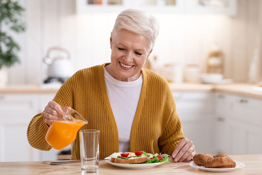 Attractive old lady pouring juice having lunch in kitchen