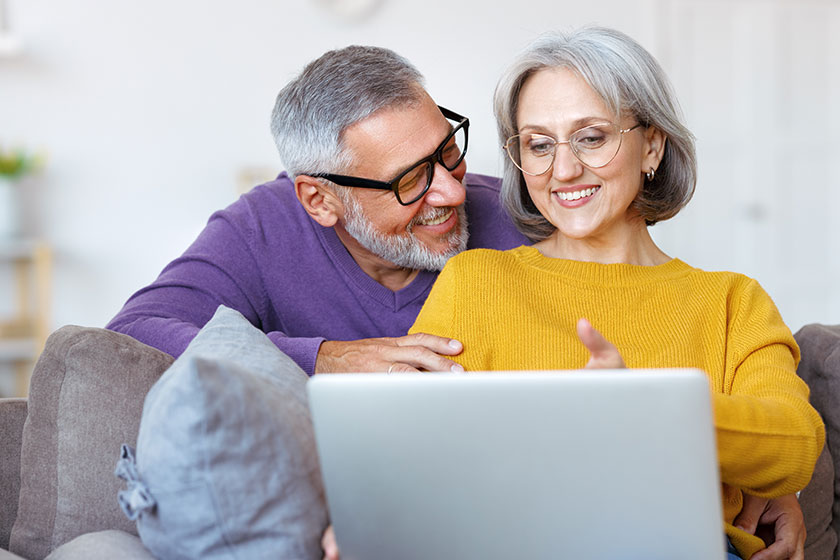 Beautiful mature family couple looking at laptop with smile on face while spending time together
