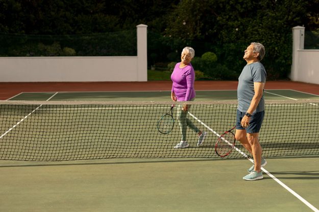 Biracial smiling senior man senior woman rackets walking net tennis