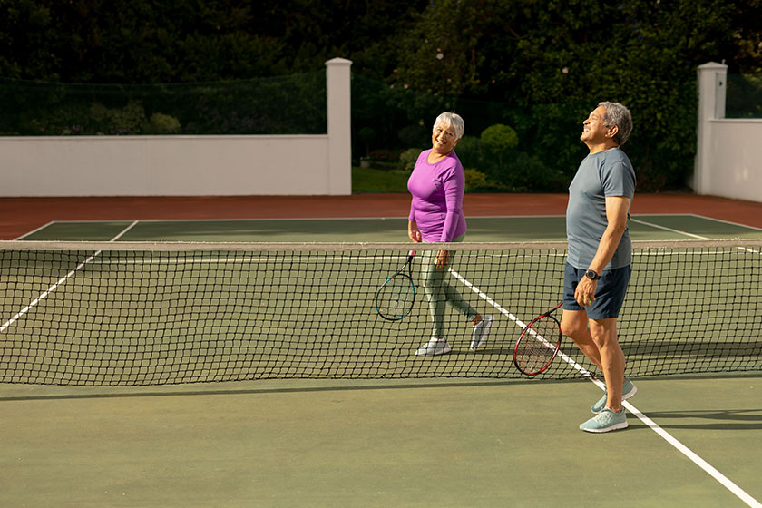 Biracial smiling senior man senior woman rackets walking net tennis Biracial smiling senior man senior woman rackets walking net tennis