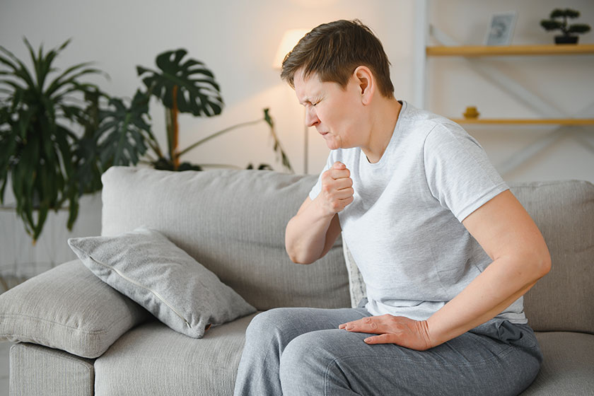 Sick adult woman coughing covering mouth tissue sitting couch home