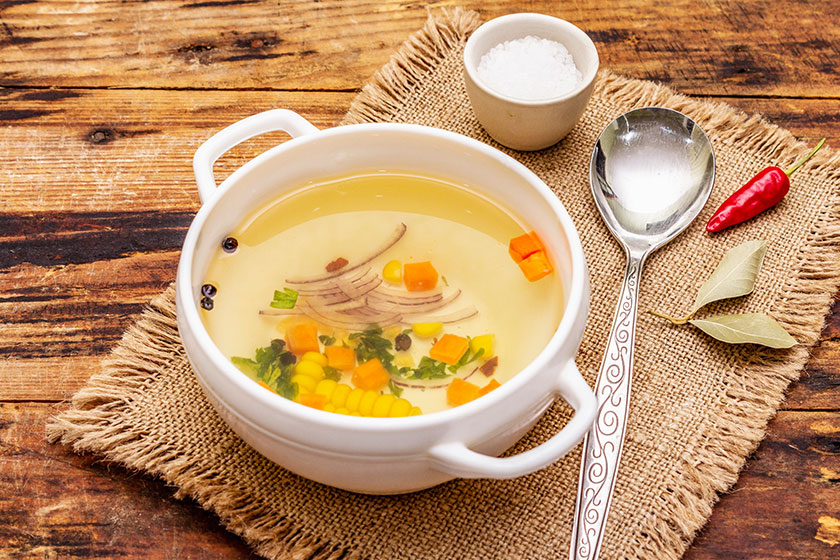 Transparent duck broth in bowl with vegetables traditional bouillon healthy meal old wooden background