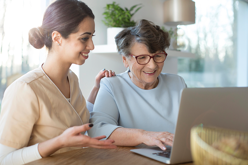 happy assistant teaching elderly woman searching internet