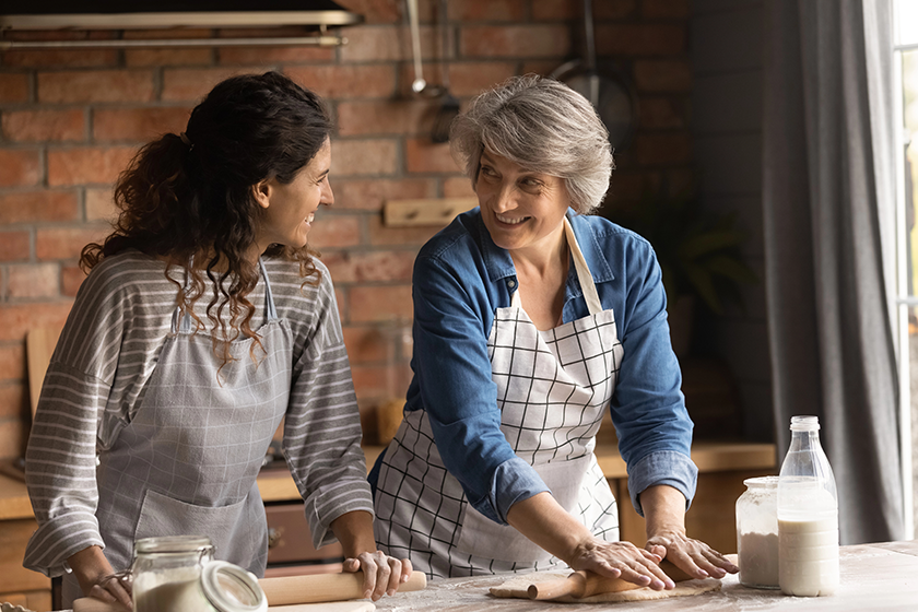 happy latin grown daughter and senior mother cooking