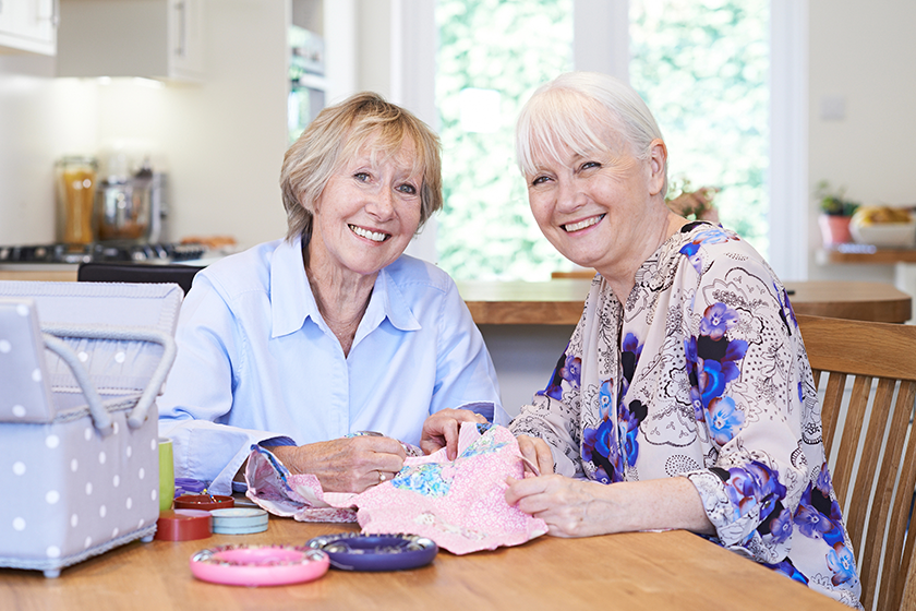 portrait of two senior women sewing quilt together