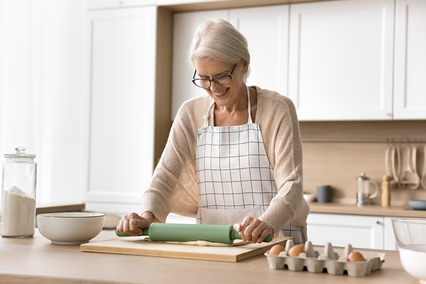 positive mature baker woman wearing apron rolling dough