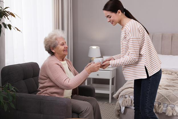 young caregiver giving tea senior woman