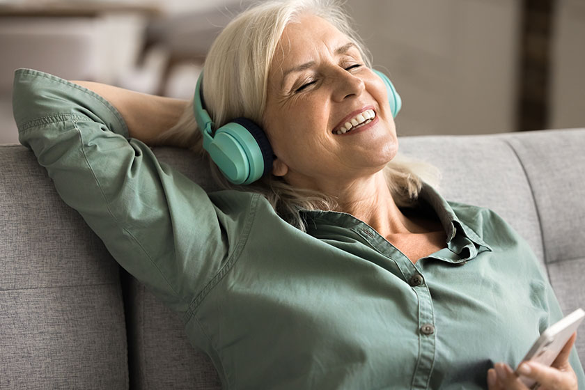 Cheerful inspired blonde elderly woman singing song home listening music