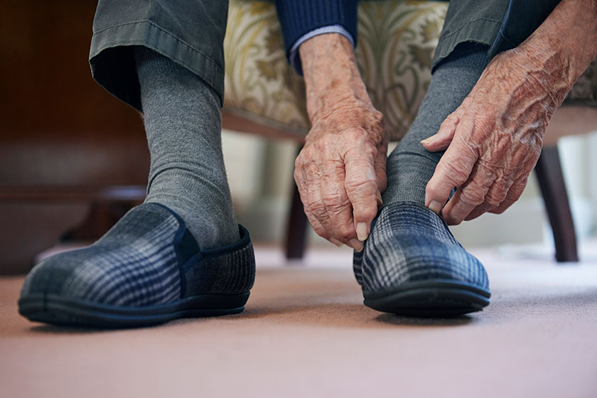 Close senior man putting slippers keep feet warm cost living