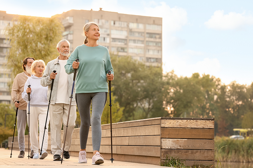 Group senior people performing nordic walking outdoors space text low