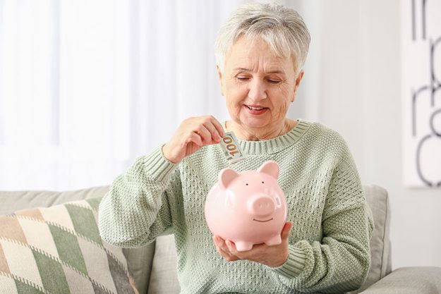 Senior woman putting money piggy bank home