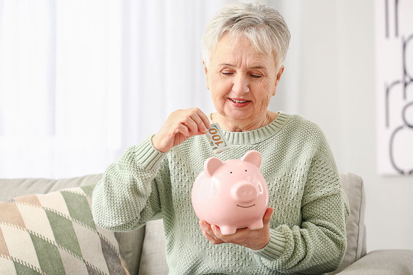 Senior woman putting money piggy bank home Senior woman putting money piggy bank home