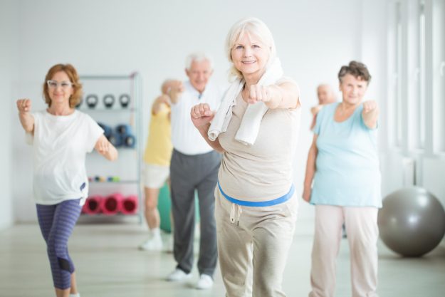Smiling,Elderly,Trainer,Exercising,With,Group,Of,Senior,People,At Smiling,Elderly,Trainer,Exercising,With,Group,Of,Senior,People,At