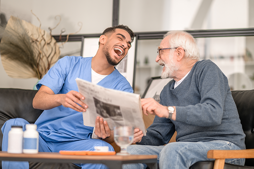 caregiver and an aged man laughing at a news
