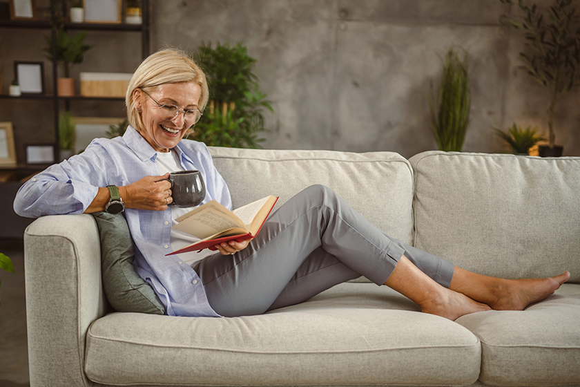 mature woman sit living room read book drink coffee