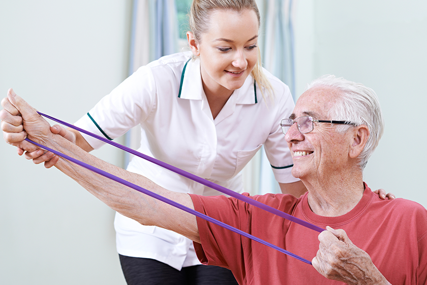 physiotherapist helping senior male to use resistance band