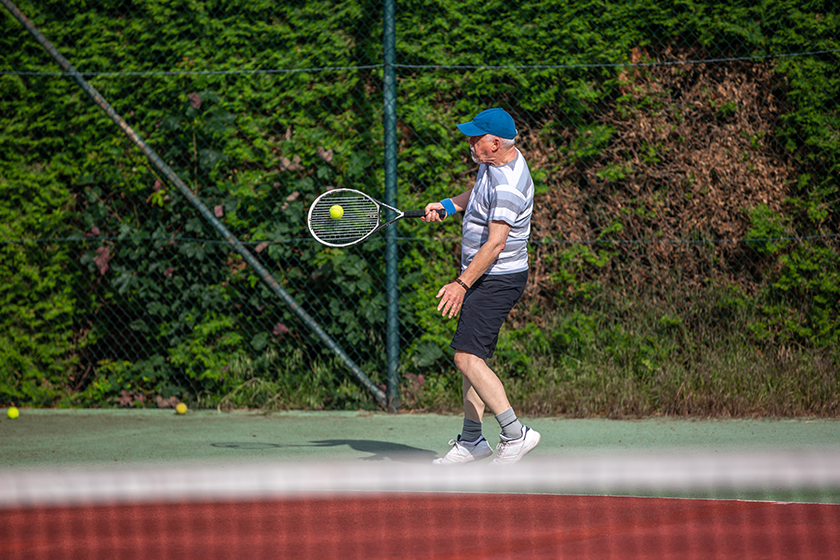 senior man playing tennis outside