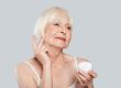 Feels good... Beautiful senior woman applying beauty product while standing against grey background