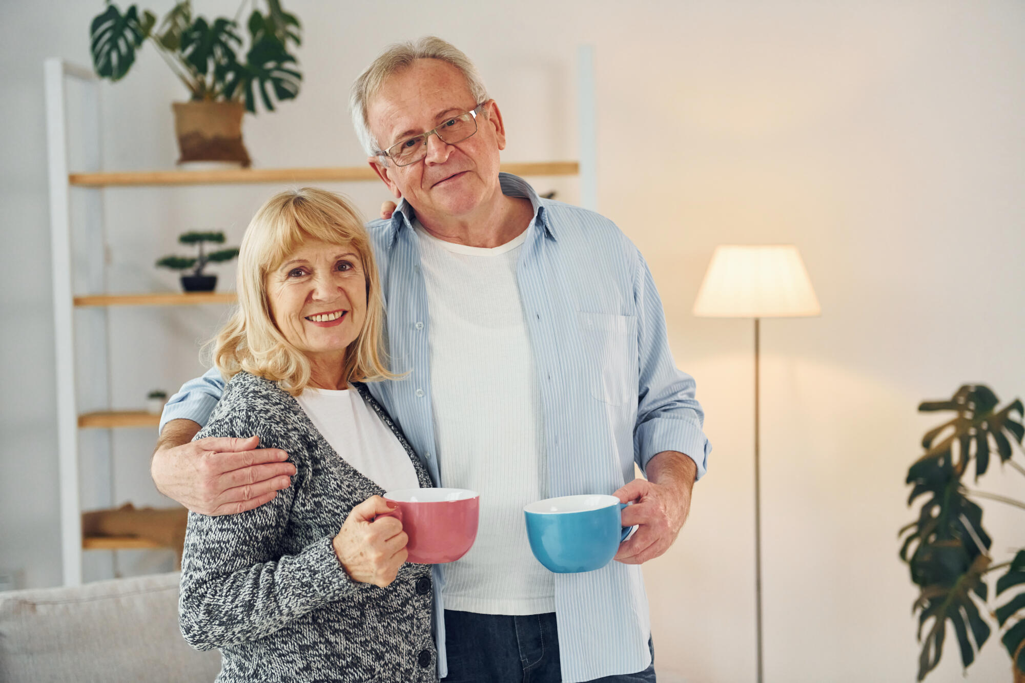 Standing and holding cups of drinks. Senior man and woman is together at home