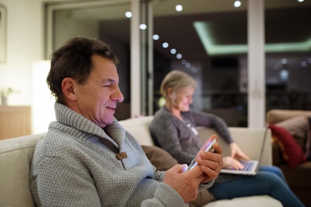 Senior,Couple,With,Laptop,And,Smartphone,Sitting,On,Couch