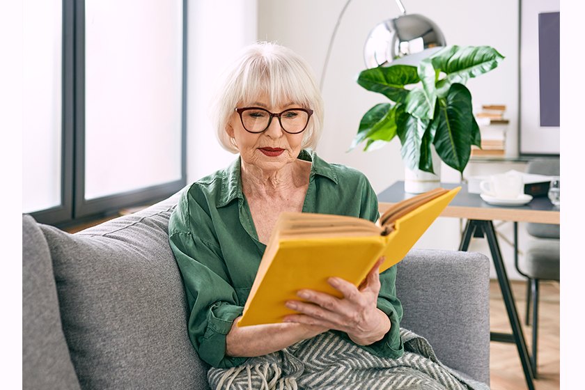 cheerful senior woman sitting couch reading book cheerful senior woman sitting couch reading book