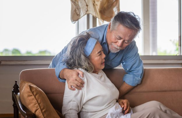 Elderly asian carrying his wife in pain lying on sofa in living Elderly asian carrying his wife in pain lying on sofa in living