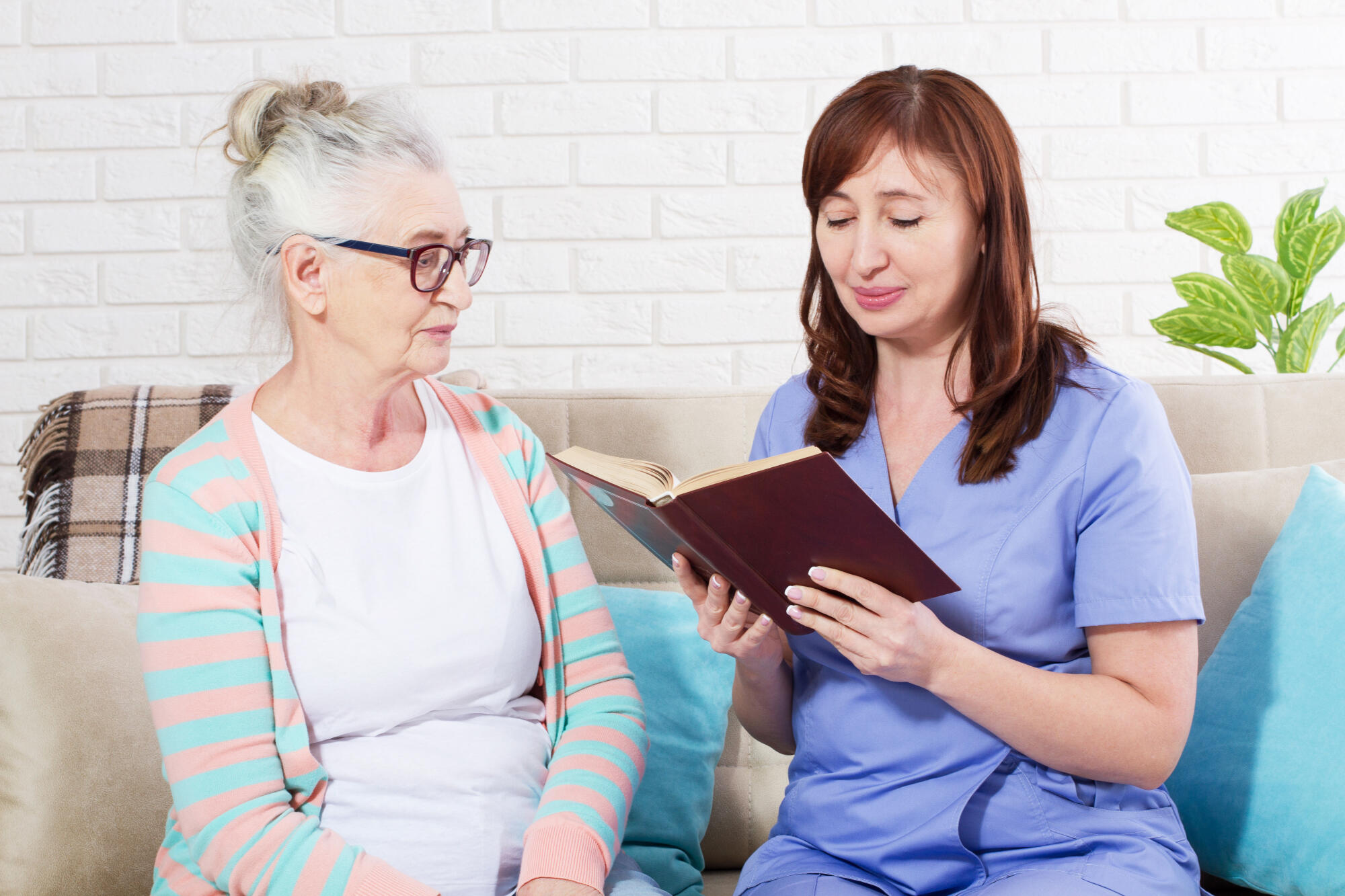 Woman reading a book to a senior citizen woman in nursing home