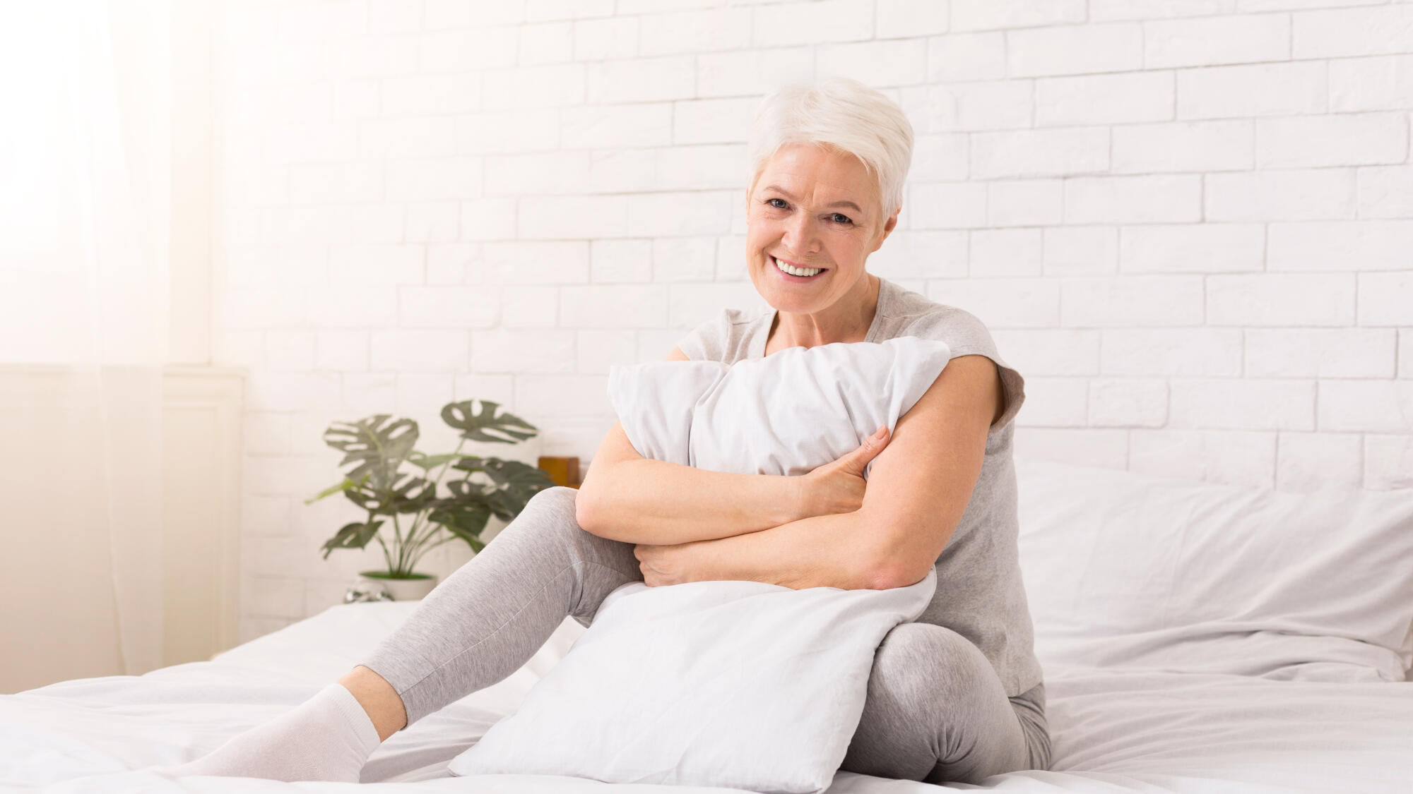 Senior woman hugging white pillow at home