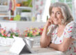 Portrait of beautiful senior woman using modern tablet while drinking tea