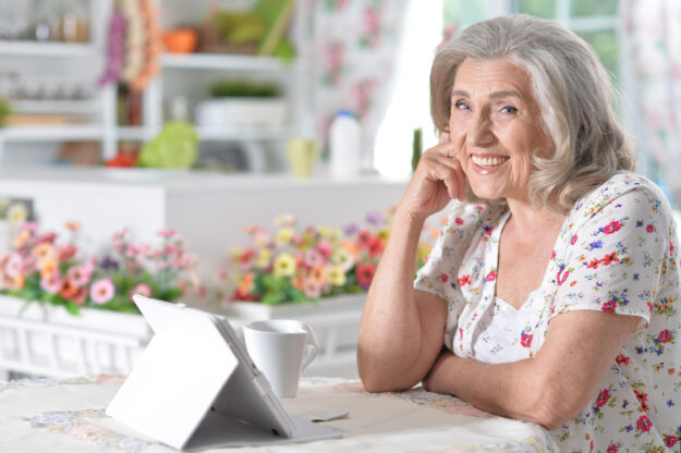 Portrait of beautiful senior woman using modern tablet while drinking tea